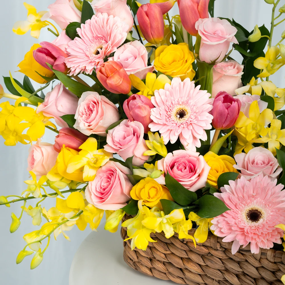 A basket arrangement of 3 pink gerberas, 15 pink roses, 5 yellow roses, 10 pink tulips and 5 stems of yellow orchids with green fillers and multi-colored easter eggs.