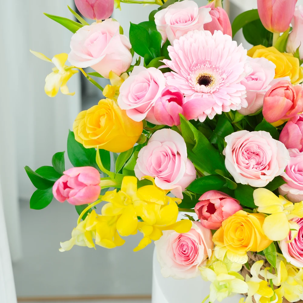 A basket arrangement of 3 pink gerberas, 15 pink roses, 5 yellow roses, 10 pink tulips and 5 stems of yellow orchids with green fillers and multi-colored easter eggs.