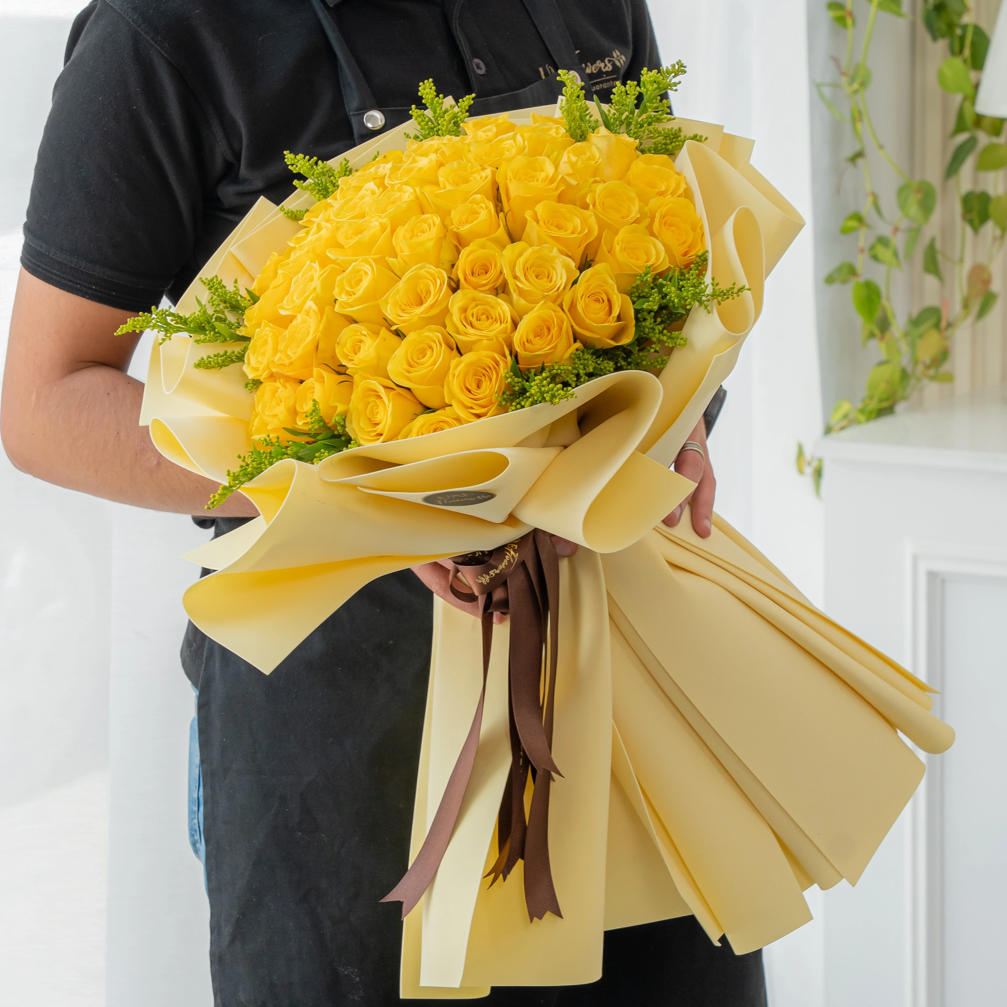 Bouquet of 40 yellow roses with solidago fillers in yellow foam paper tied with ribbons.