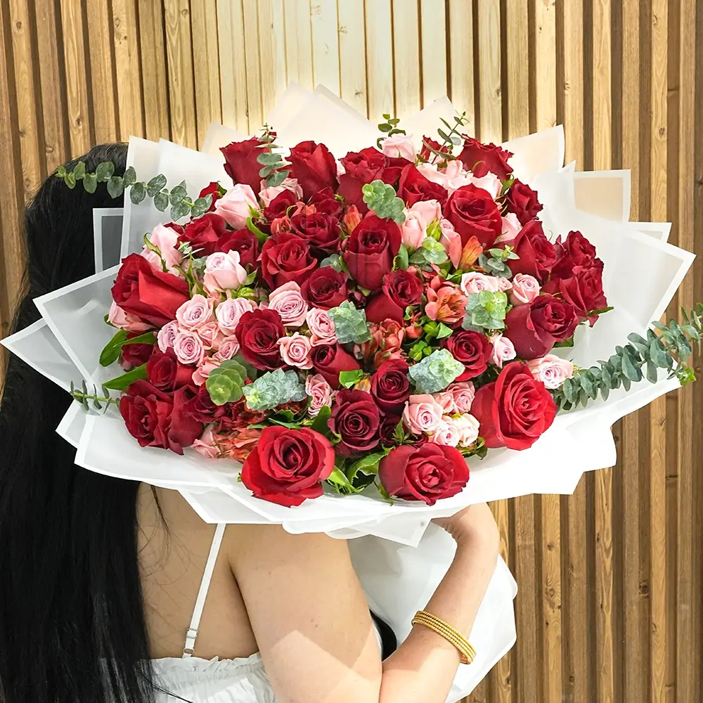 A bouquet of 20 red roses, 5 pink spray roses, and 2 red alstroemeria with eucalyptus leaves and green fillers in white wrapping paper tied with white ribbons