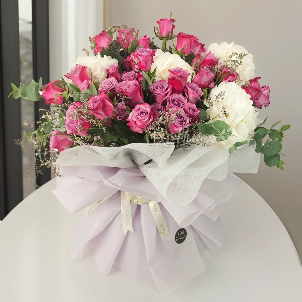 A bouquet of 4 white hydrangeas and 40 purple roses with green and limonium fillers in purple wrapping paper tied with white ribbon