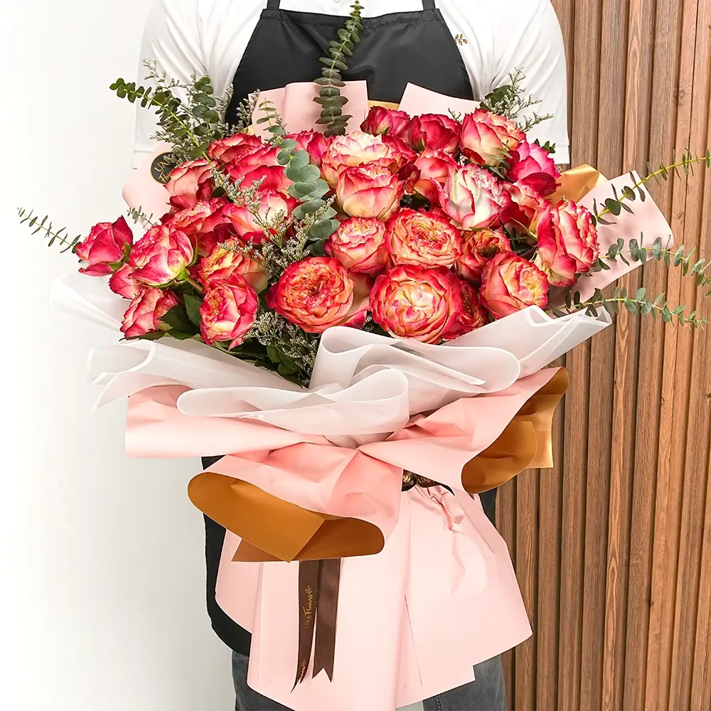 A bouquet of red double-color applejack garden roses with eucalyptus leaves in pink wrapping paper tied with a brown ribbon