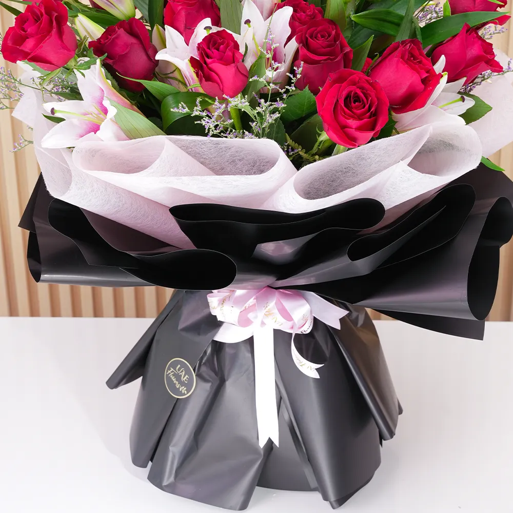 A bouquet of 4 pink lilies & 10 red roses in pink wrapping paper tied with a pink ribbon
