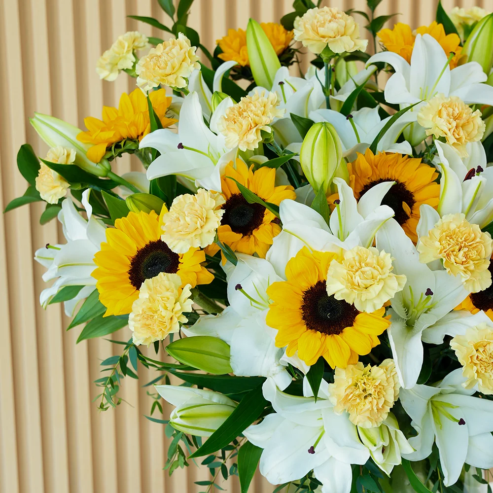 15 white lilies, 10 sunflowers & 20 peach carnations in a glass vase