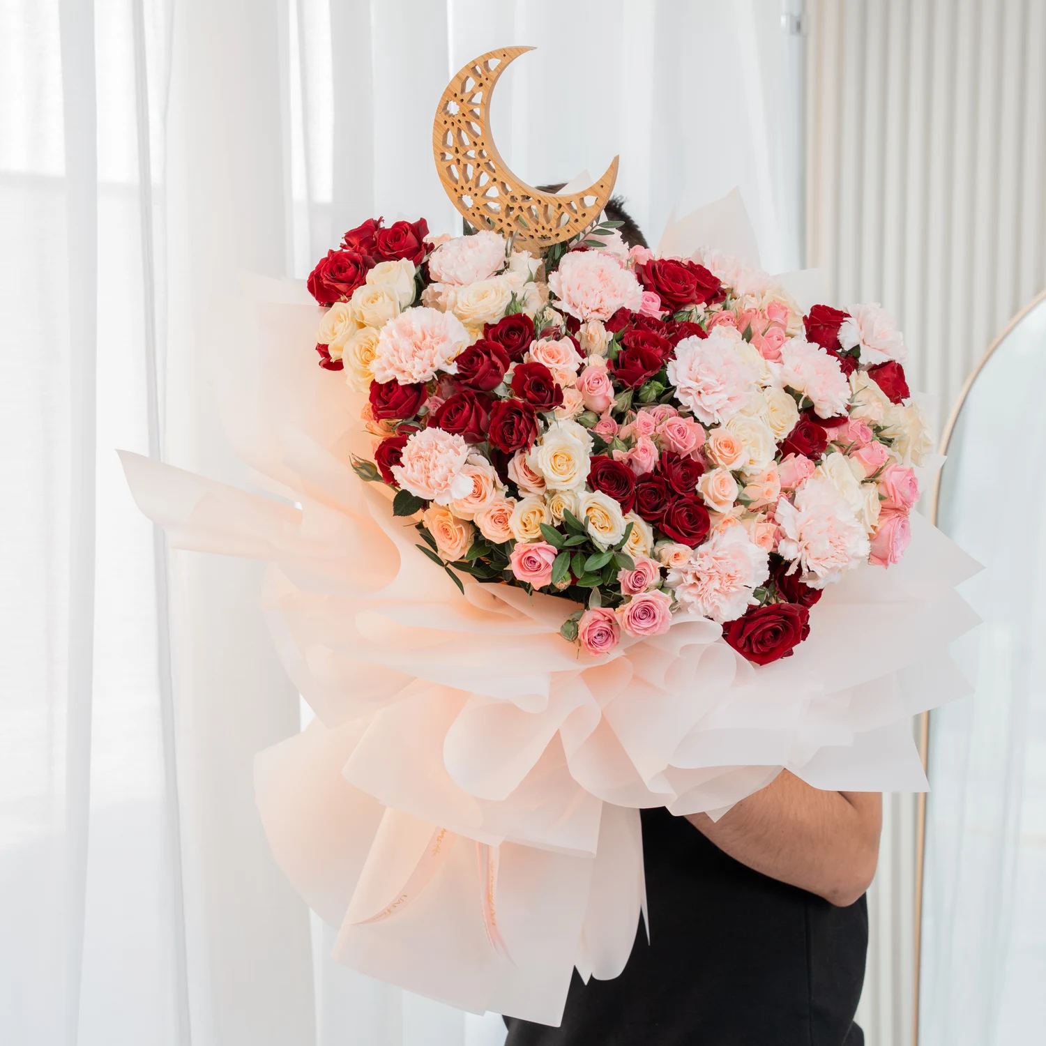 Moonlit bouquet with red, pink, and peach spray roses, pink carnations, and a gold crescent moon topper, wrapped in soft beige fabric – elegant Ramadan floral gift by UAE Flowers.