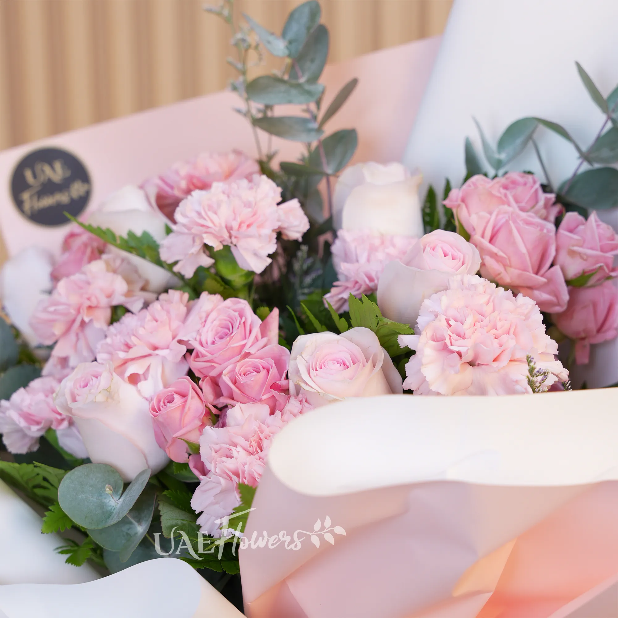 bouquet with 5 pink roses, 7 carnations, and 4 pink spray roses. Wrapped in paper with ribbons and green fillers.