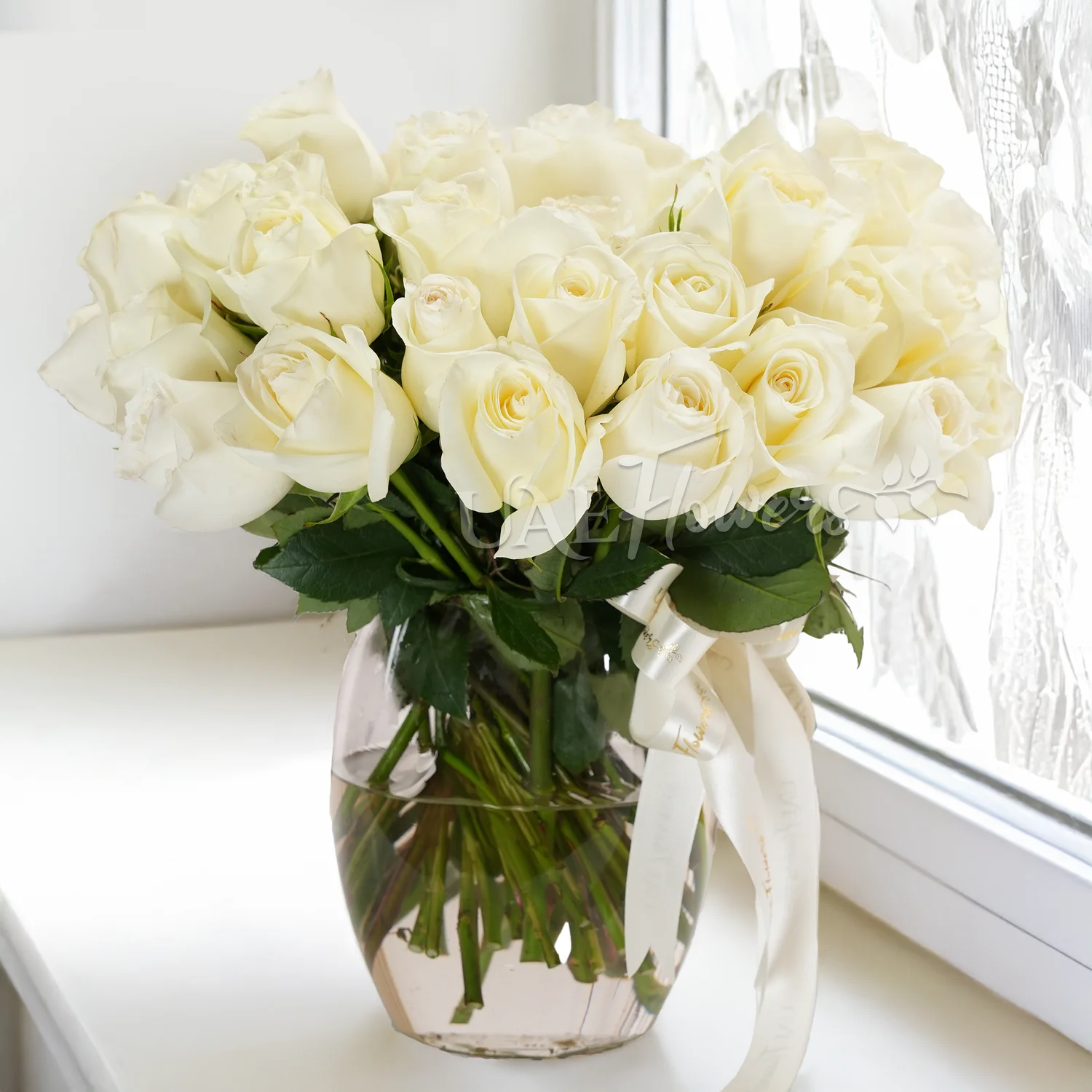 Glass vase with 40 white roses, green fillers, and a delicate white ribbon.