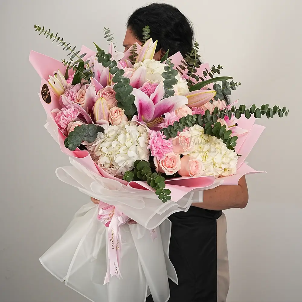 A bouquet of 3 white hydrangeas, 2 pink lilies, 12 pink roses, 10 pink carnations with eucalyptus leaf and green fillers in pink and white wrapping paper tied with pink ribbon
