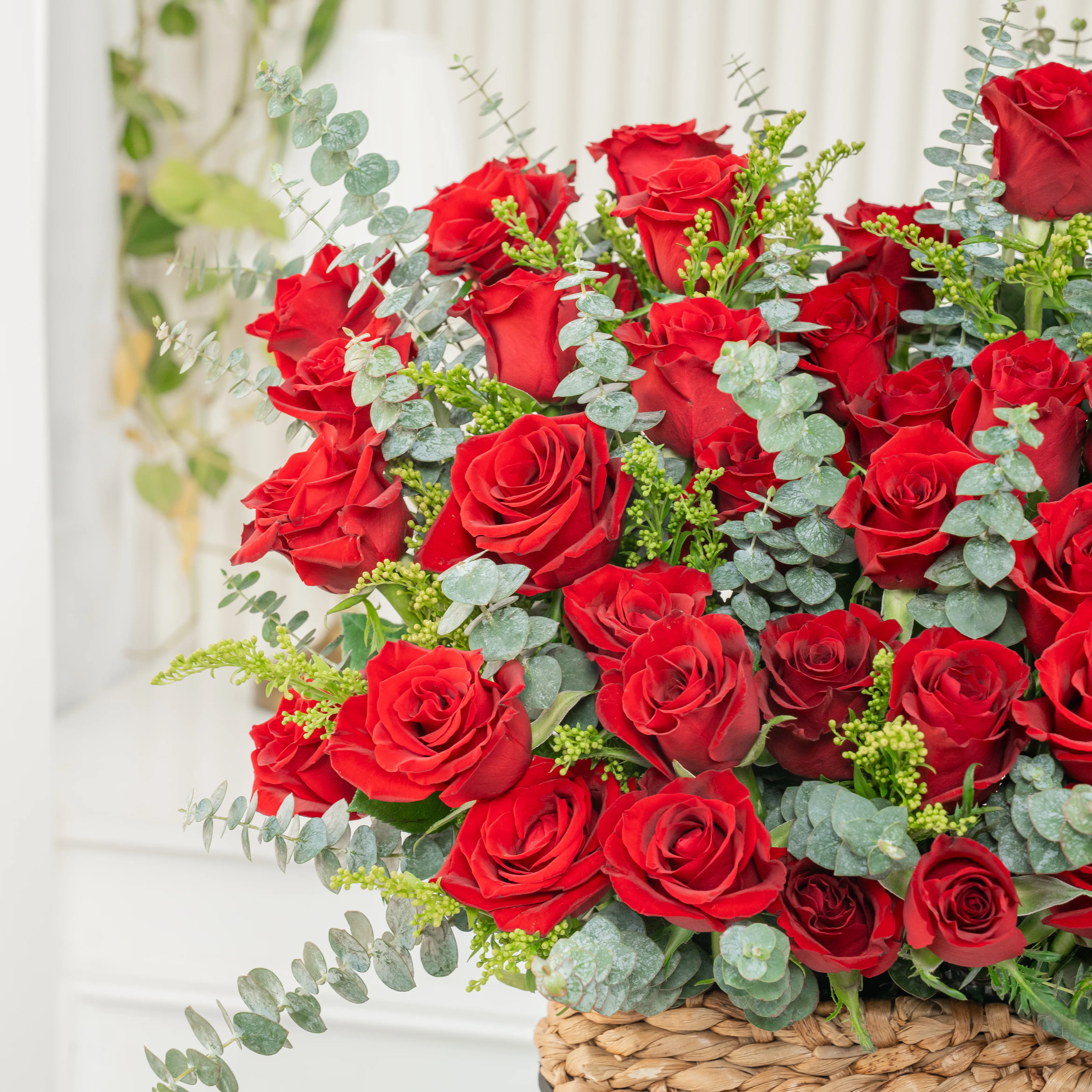 40 red roses with eucalyptus leaf in a square basket.