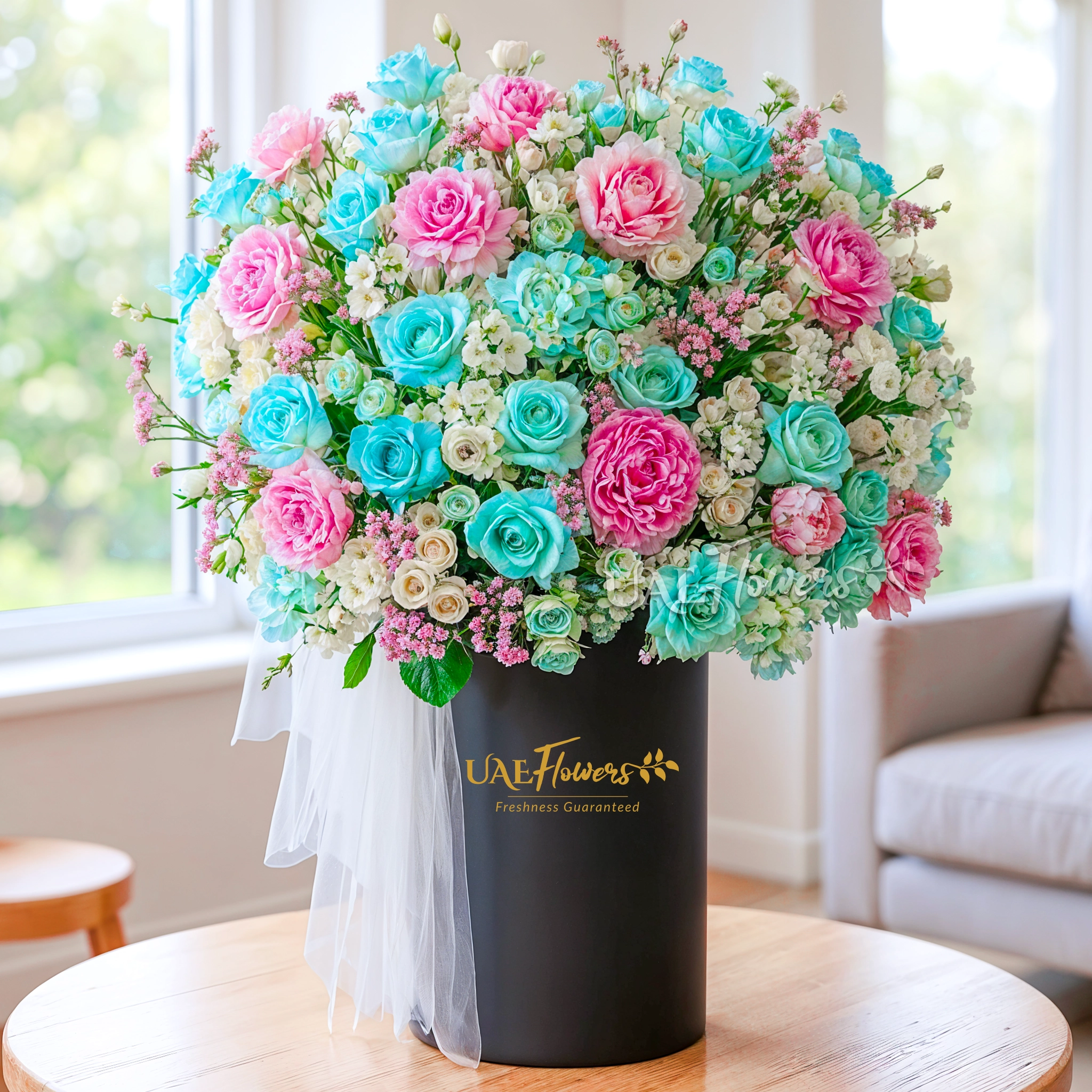 An arrangement of pink peonies, blue hydrangeas, blue color roses, white matthiola and white and blue spray roses with green fillers and white net in a tall round box.