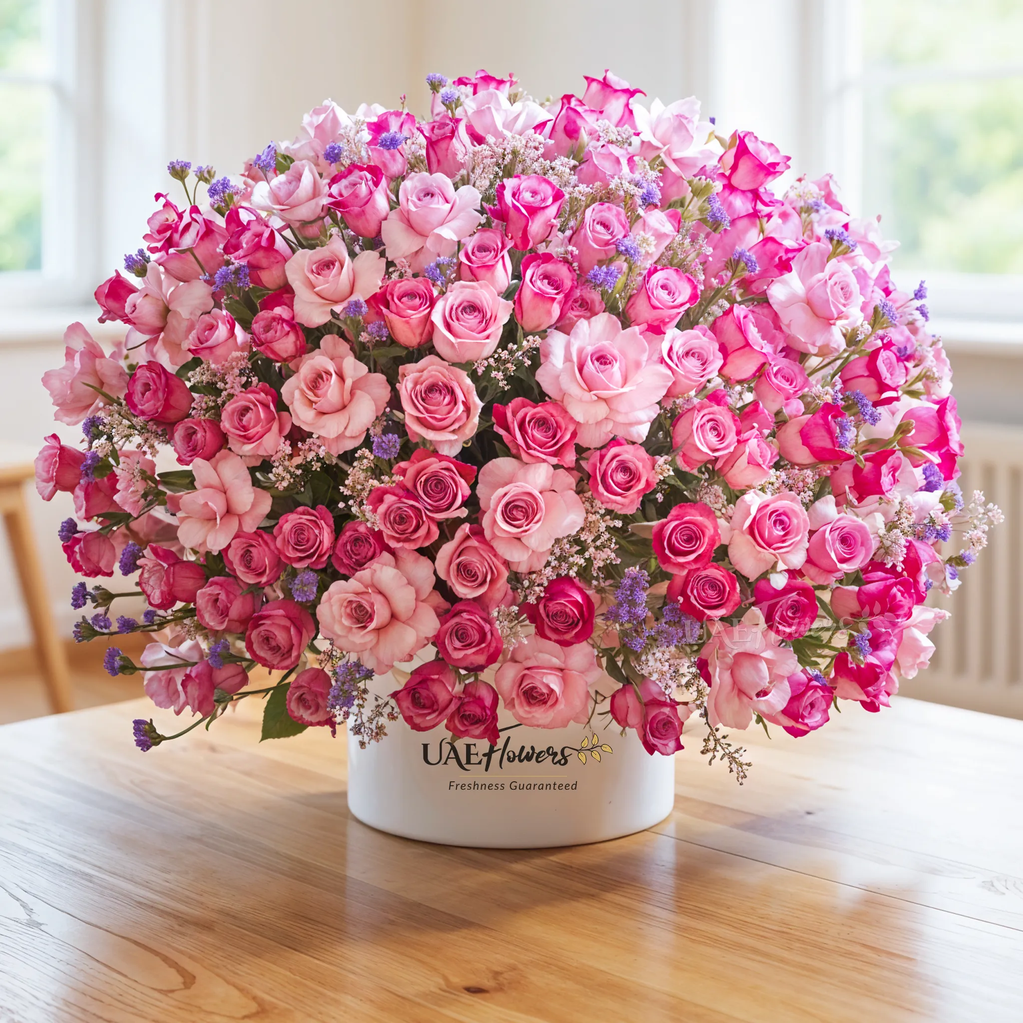A half round arrangement of 100 purple roses, statice flowers with a lot of greens, & eucalyptus leaves in a round white box