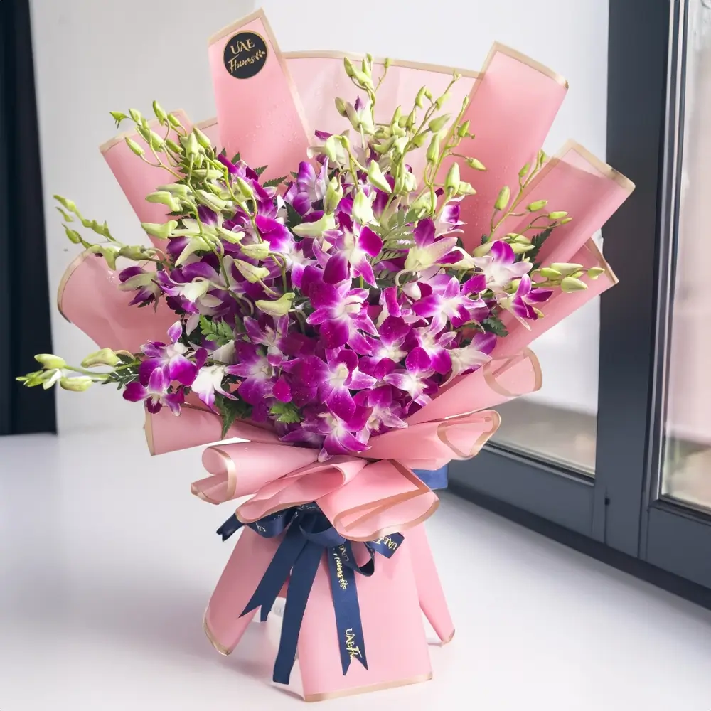 A bouquet of purple orchids with green fillers wrapped in pink paper tied with blue ribbons