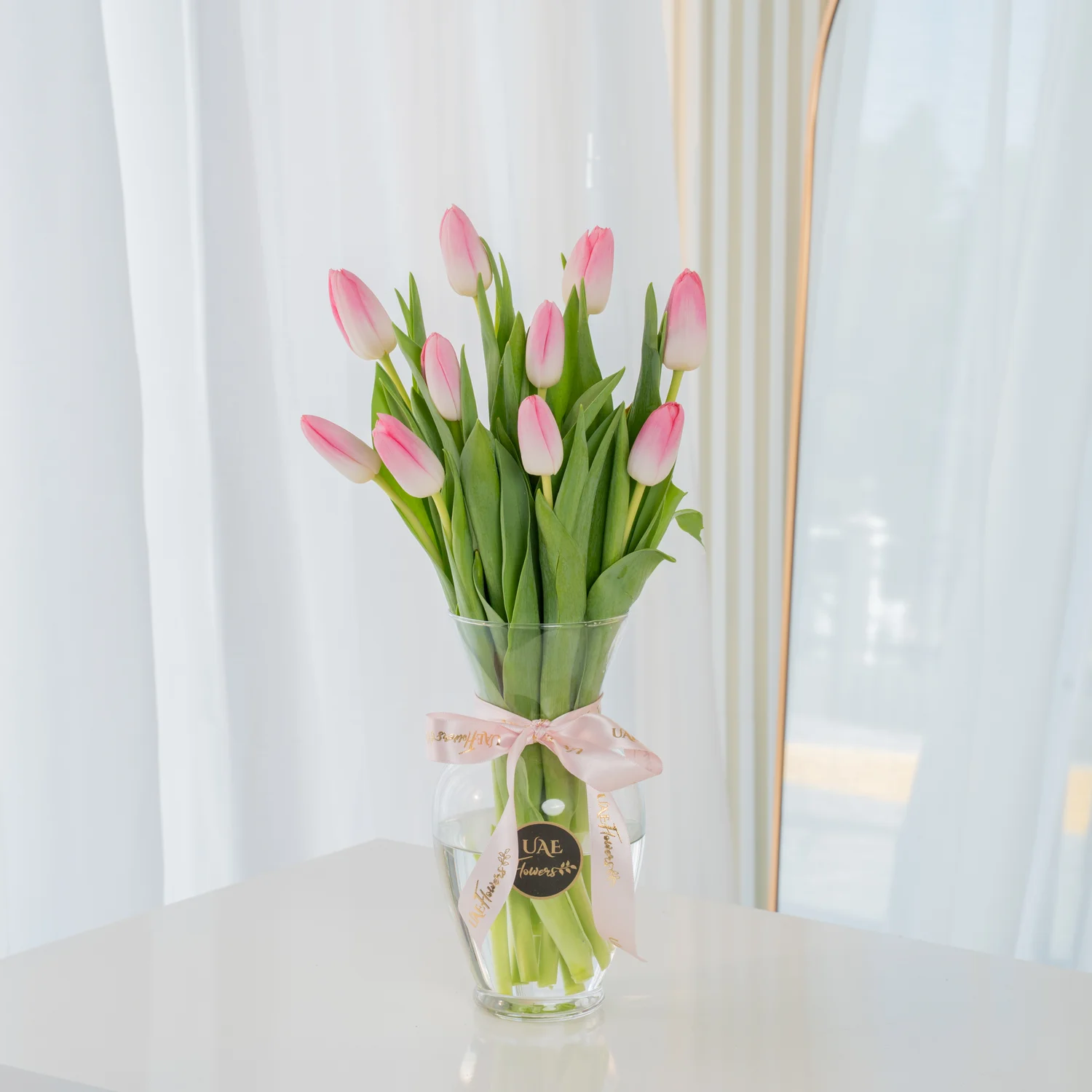 10 pink tulips in a glass vase tied with ribbons.