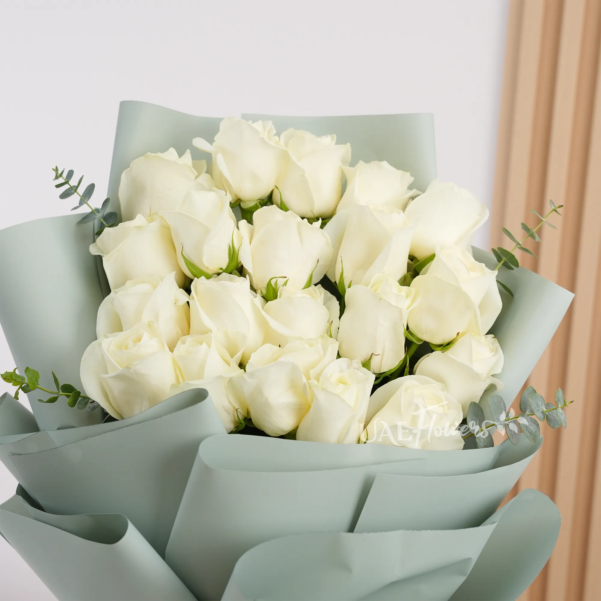 Bouquet of 20 white roses with green fillers wrapped in soft paper and tied with white ribbon, perfect for weddings, anniversaries, and special occasions.